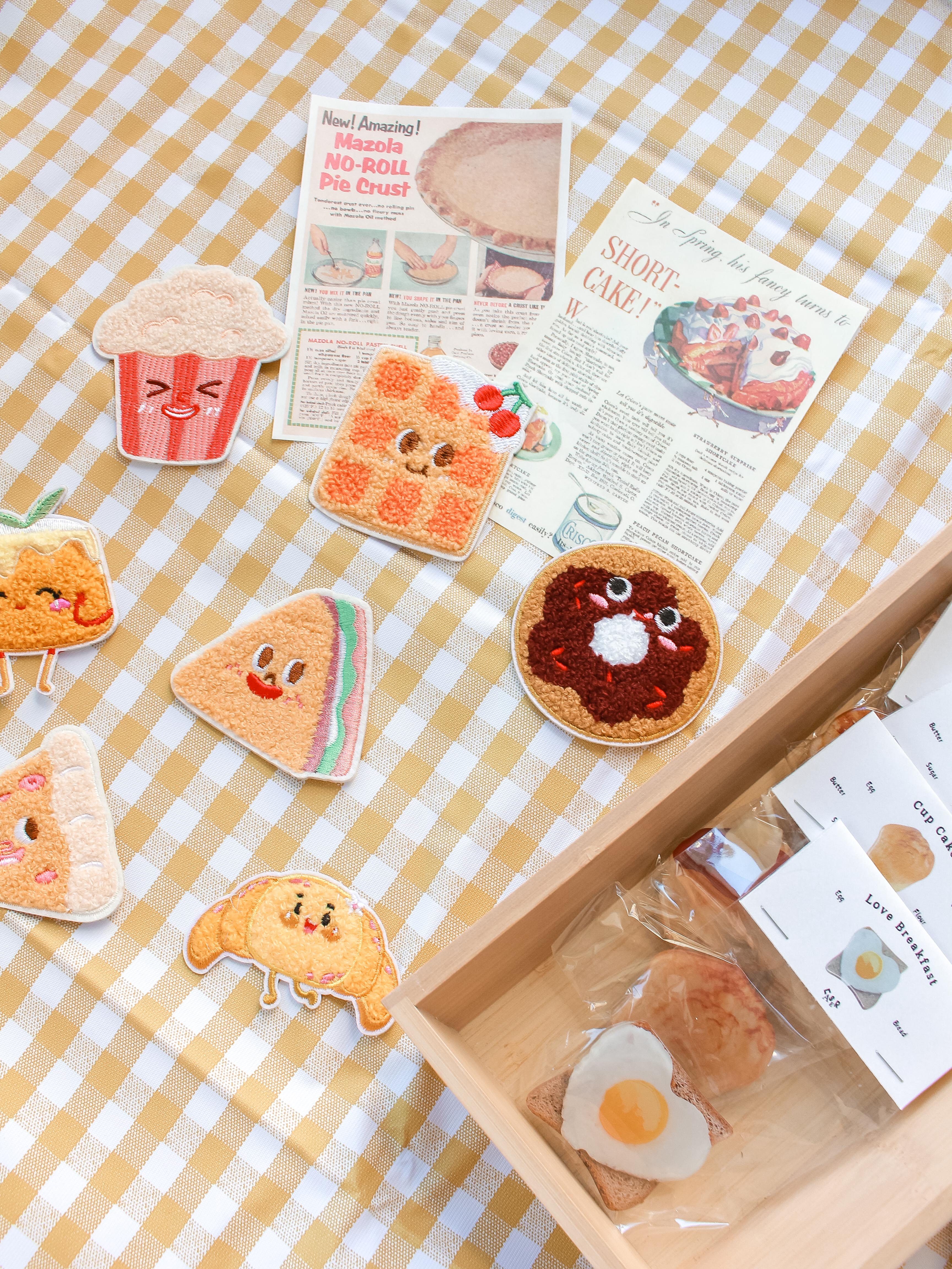 Set of cute food-themed cookies patch stickers on a checkered tablecloth with a box of additional food-themed phone grips