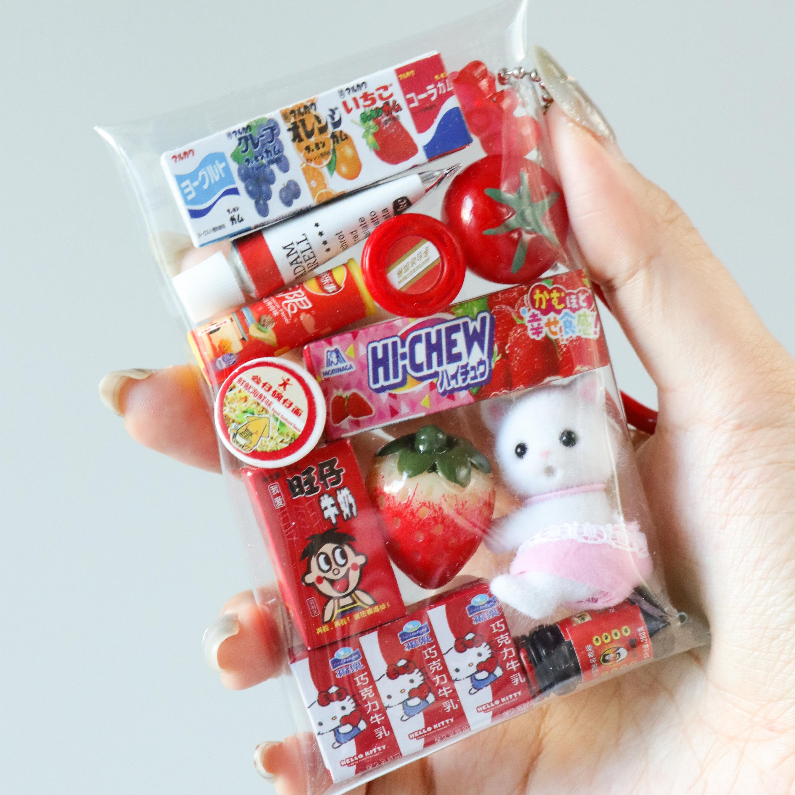 Hand holding a "gacha-style" bag charm with mini food-theme toy in red on a light gray background.