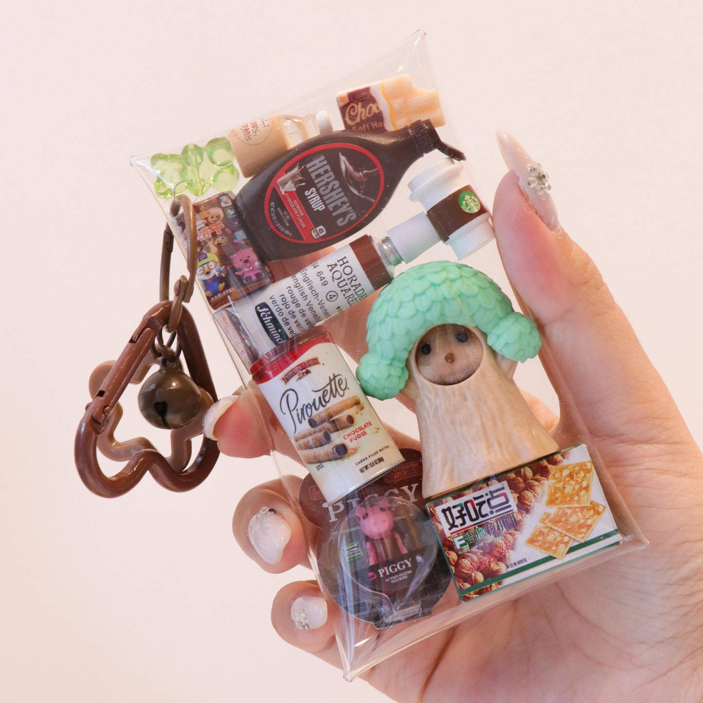 Hand holding a keychain with various miniature product packaging on a light background