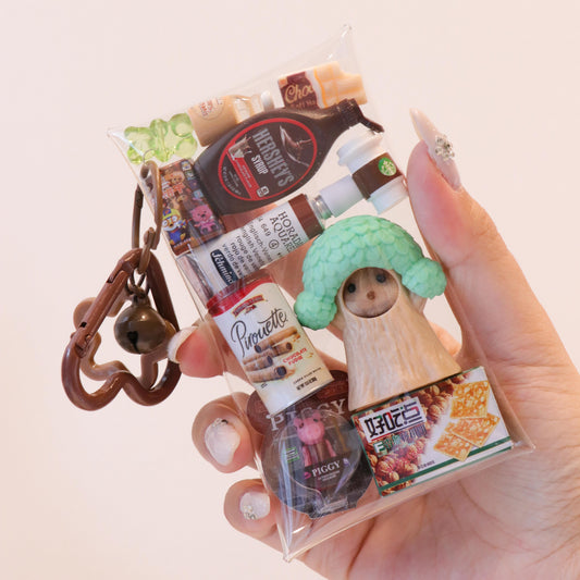 Hand holding a keychain with various miniature product packaging on a light background