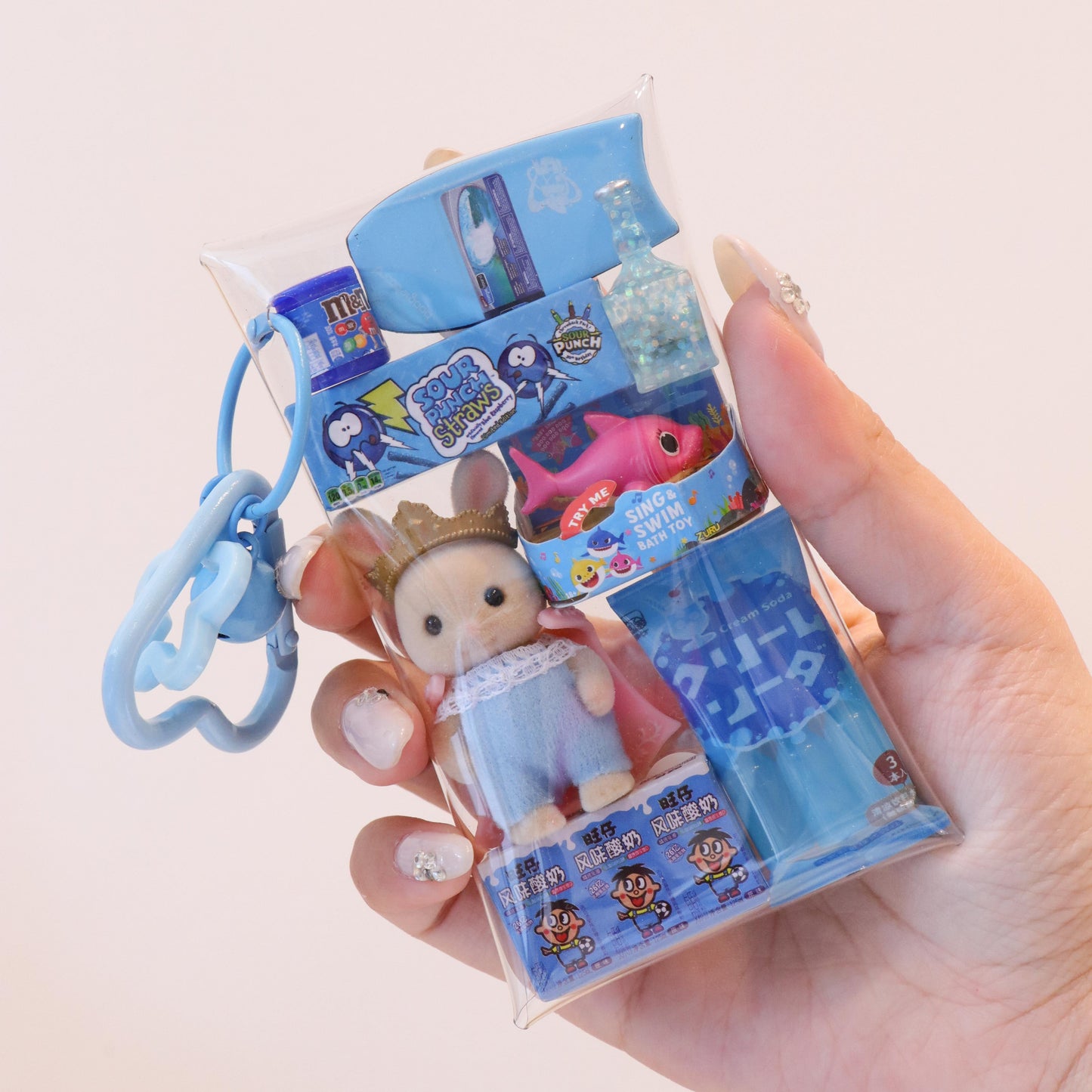 Hand holding a small toy figure with packaging featuring cartoon characters on a light pink background