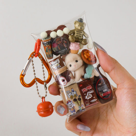 Hand holding a clear plastic bag with small toys and decorative items against a light gray background